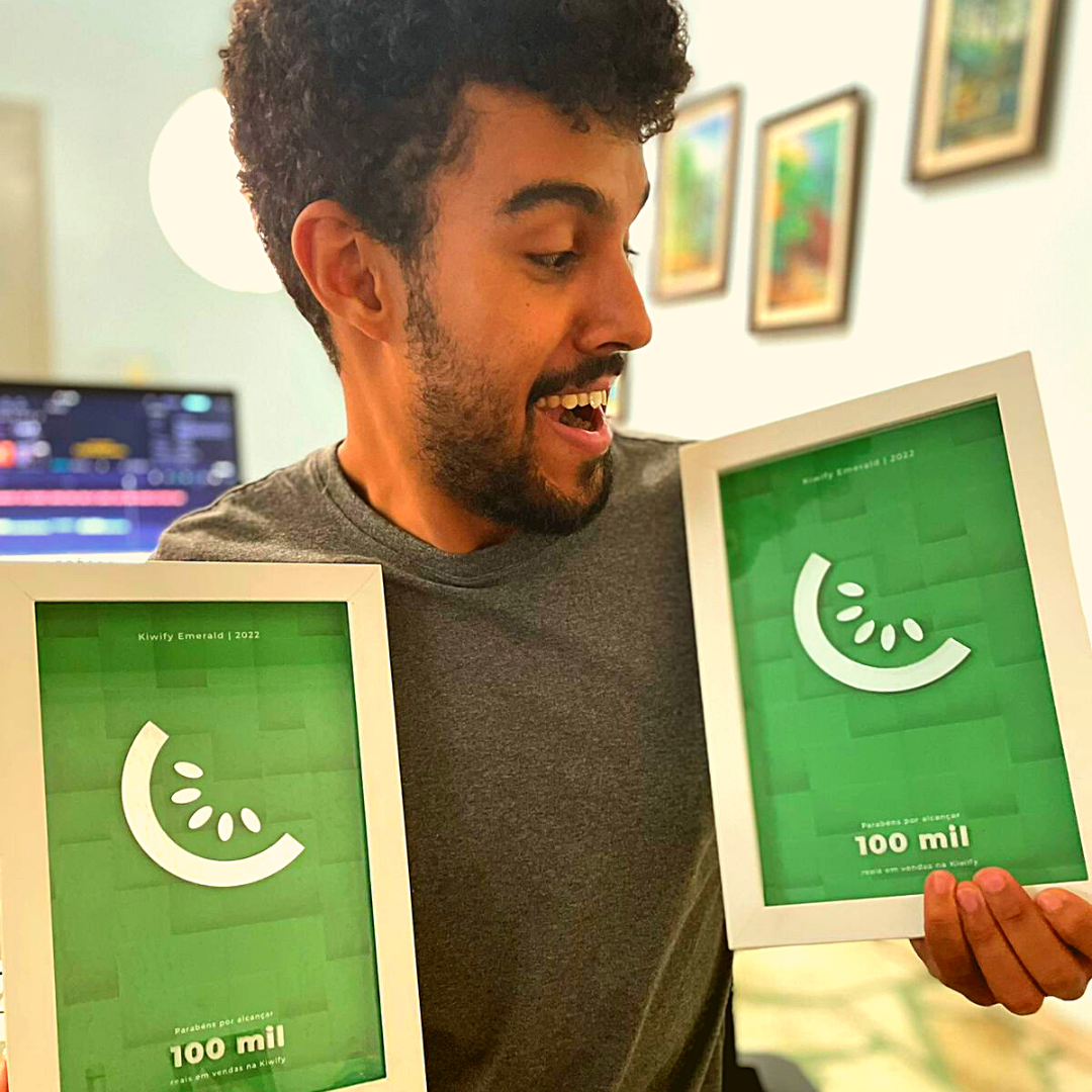 Léo segurando duas placas Kiwify de 100 mil reais em vendas